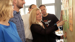 Eine Frau präsentierte einer Gruppe Zettel auf einer Pinnwand.