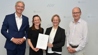 Gruppenbild mit der neuen Professorin, die stolz ihre Urkunde in den Händen hält und lächelt.
