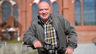 Mann lehnt sich an ein Fahrrad und lächelt.