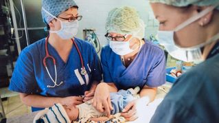 Drei OP-Schwestern stehen um ein Baby herum.