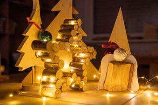 Leuchtender Weihnachtsstern aus Holz, daneben steht ein Holzengel und im Hintergrund sind Weihnachtsbäume