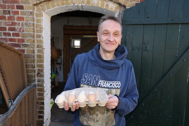 Mann lächelt und hält einen Karton mit Eiern.
