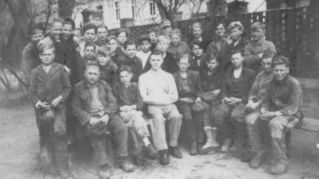 Historisches Bild zeigt Kinder und junge Männer, die im Hof sitzen.