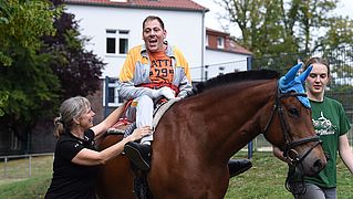 Mann sitzt auf einem Therapiepferd und lacht