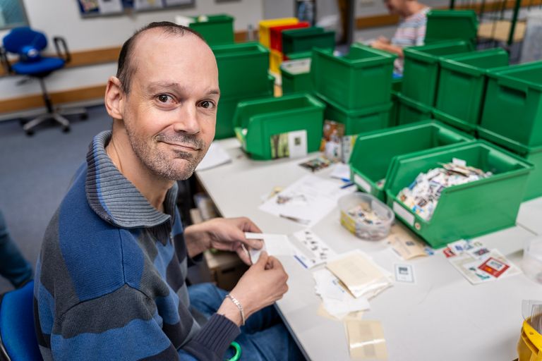 Carsten Hirsch sitzt an seinem Arbeitsplatz und sortiert Briefmarken