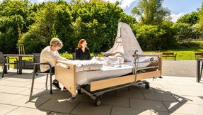 Zwei Frauen sitzen am Bett eines Gastes, das auf die Terrasse gestellt wurde.