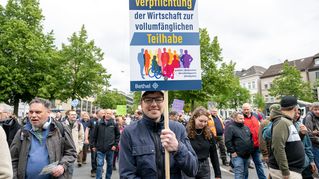 Ein Mann hält sein Plakat hoch, auf dem er die Wirtschaft zur Teilhabe verpflichten möchte.