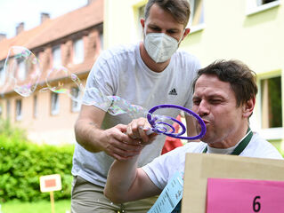 Man blows soap bubbles, employee assists in holding the handle.