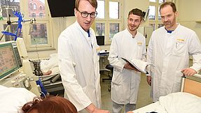 Three doctors on rounds at the hospital bedside.