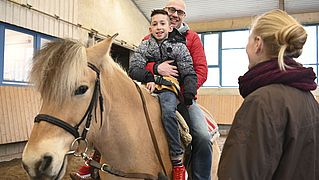 Jonas und sein Vater lächeln auf dem Pferd sitzend in die Kamera. 