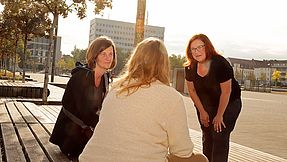 Streetworkerinnen beraten Frau auf einer Bank in der Stadt.