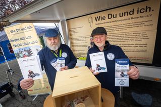Zwei Männer stehen mit Prospekten am Stand der Wohnungslosenselbstvertretung.