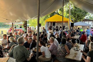 Menschen sitzen auf Bierzeltgarnituren und unterhalten sich.
