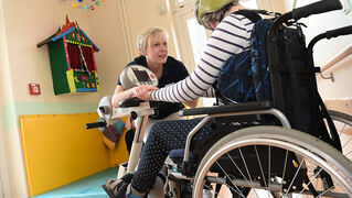 Eine Bethel-Mitarbeiterin unterstützt eine epilepsiekranke Person, die im Rollstuhl sitzt.