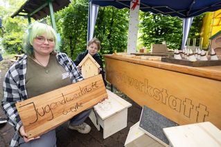 Junge Frauen präsentieren ihre Holzprodukte aus der Jugendwerkstatt an einem Stand.