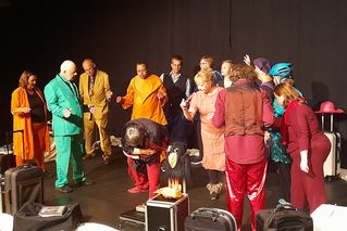 Schauspielerinnen und Schauspieler in bunten Kostümen führen ein Theaterstück auf.