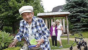 Mitarbeiterin betreut zwei Seniorinnen im Garten.