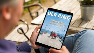 Ein Mann sitzt an einem Tisch und schaut auf das RING-Titelbild auf einem Tablet