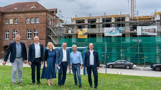 Diakon Wolfgang Roos-Pfeiffer von der Direktion Sarepta/Nazareth, Bethels stellvertretender Vorstandsvorsitzender Pastor Dr. Bartolt Haase, die Bethel.regional-Geschäftsführer Sandra Waters und Stefan Helling-Voß, Rolf Wacker, Leiter Immobilien Bethel.regional, und Architekt Sven Grüne stehen vor der Baustelle.