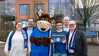 Drei Männer, ein Junge und eine Frau lächeln zusammen mit einem Maskottchen in die Kamera