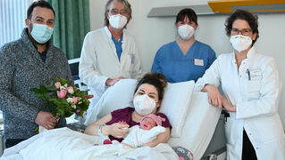 Foto der Neugeborenen mit Eltern, Ärzten und Hebamme im Krankenzimmer