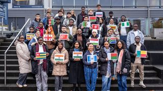 Junge Menschen stehen auf einer Treppe und halten verschiedenen Landesflaggen in den Händen. 