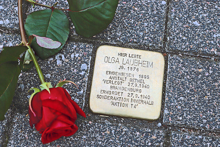Ein Rose liegt neben einem Stolperstein.
