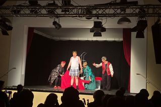 Schauspielerinnen und Schauspieler führen auf der Bühne in Kostümen ein Stück auf.