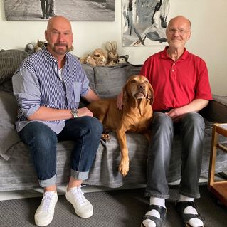 Ralf Knorr und Markus Prummer sitzen mit Hund Paul auf einer Couch in ihrer WG.