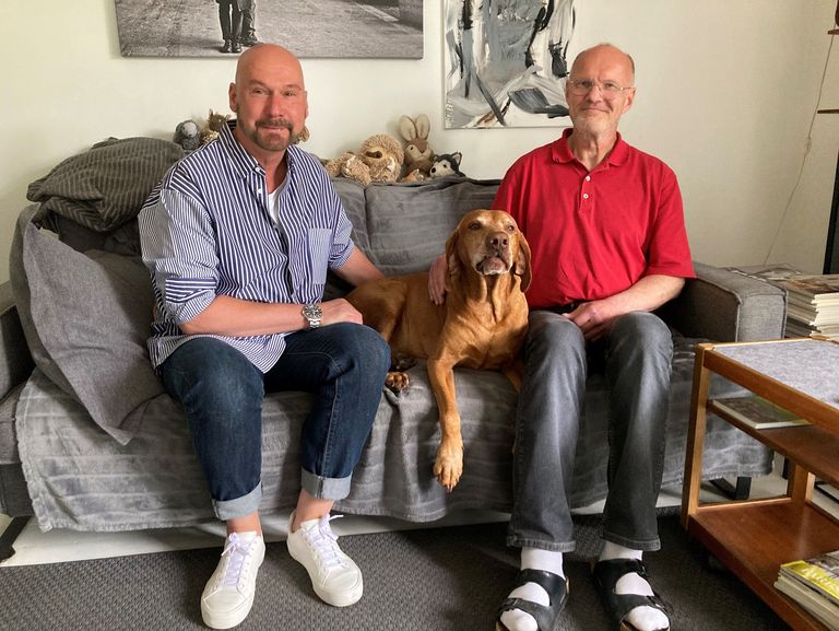 Ralf Knorr und Markus Prummer sitzen mit Hund Paul auf einer Couch in ihrer WG.