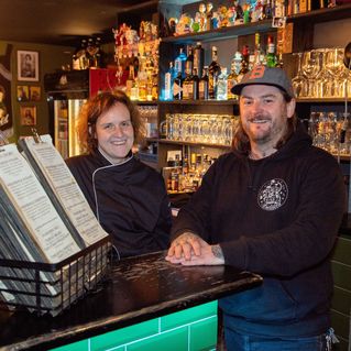 Sonja Schüler und Benjamin Stücke stehen an der Bar und lächeln in die Kamera