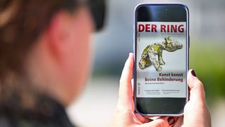 Eine Person mit Sonnenbrille hält ein Smartphone mit der digitalen Juni-Ausgabe von DER RING in den Händen