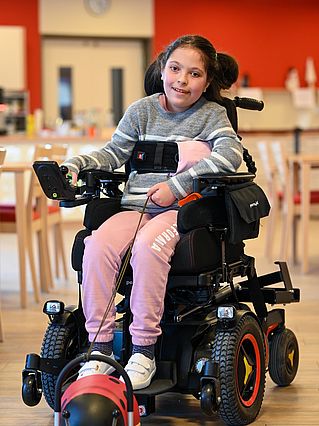 Lächelndes Mädchen aus Kinderhospiz in elektrischem Rollstuhl