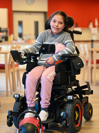 Lächelndes Mädchen aus Kinderhospiz in elektrischem Rollstuhl