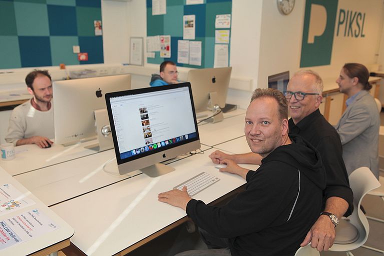 Vier Männer und eine Frau sitzen an einem Schreibtisch. Auf dem Schreibtisch stehen vier Computer.
