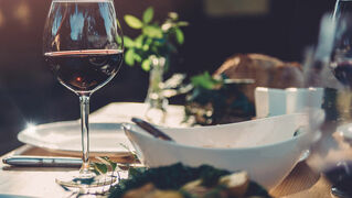 Festlich gedckter Tisch mit einem Glas gefüllt im Rotwein im Vordergrund