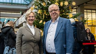 Prof. Dr. Angelika Epple und Pastor Ulrich Pohl stehen vorm Baum in der Unihalle.
