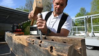 Zimmermann Sven Krökel arbeitet den historischen Engeltorbogen aus Bethel mit Klopfholz und Stemmeisen auf.