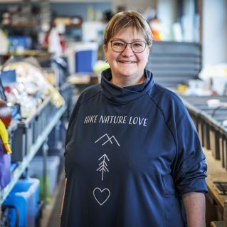 Heike Szillmischkies lächelt in die Kamera. Hinter ihr sind viele Boxen mit Klamotten.