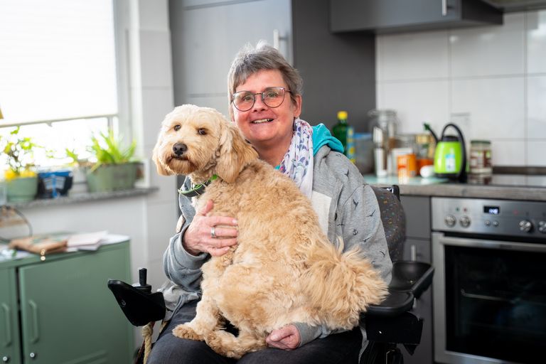Ursula Niggemeier sitzt in ihrer Küche im Rollstuhl, auf ihrem Schoß sitzt ihr Hund Toffi