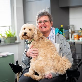 Ursula Niggemeier sitzt in ihrer Küche im Rollstuhl, auf ihrem Schoß sitzt ihr Hund Toffi