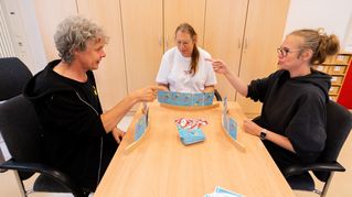 Drei Personen spielen an einem Tisch das Kartenspiel UNO.