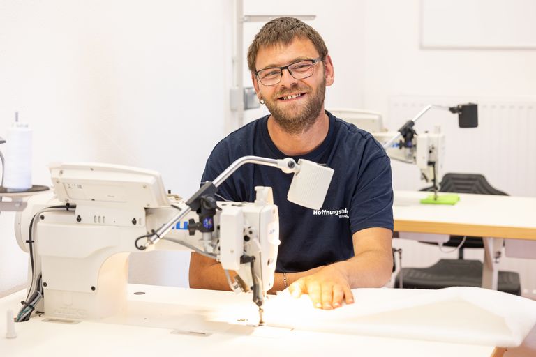 Patrick Engel sitzt an der Nähmaschine und lächelt in die Kamera.