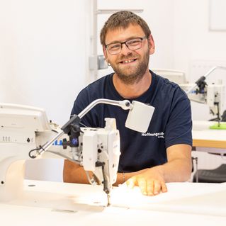 Patrick Engel sitzt an der Nähmaschine und lächelt in die Kamera.