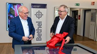 Pit Clausen und Pastor Ulrich Pohl schneiden gemeinsam ein rotes Band durch.