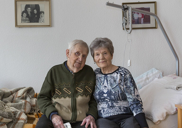 Heinz und Brigitte Müller sitzen auf ihrem Bett.