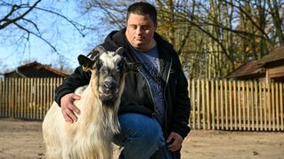 Angelo Napoletano hockt neben einer Ziege und streichelt sie am Rücken.