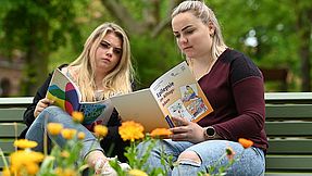 Two women on a bench look at brochures.