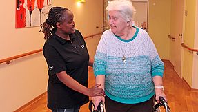 Carer accompanies senior citizen across the corridor.