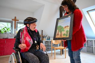 Bethel Mitarbeiterin zeigt Sylvia Straube ein gemaltes Bild im Rahmen.